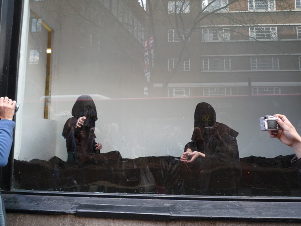 p1000534 This 2 in hooded robes are art students showcasing their arty farty abstract art in a shopping window. The brown stuff appears to be fine dirt.